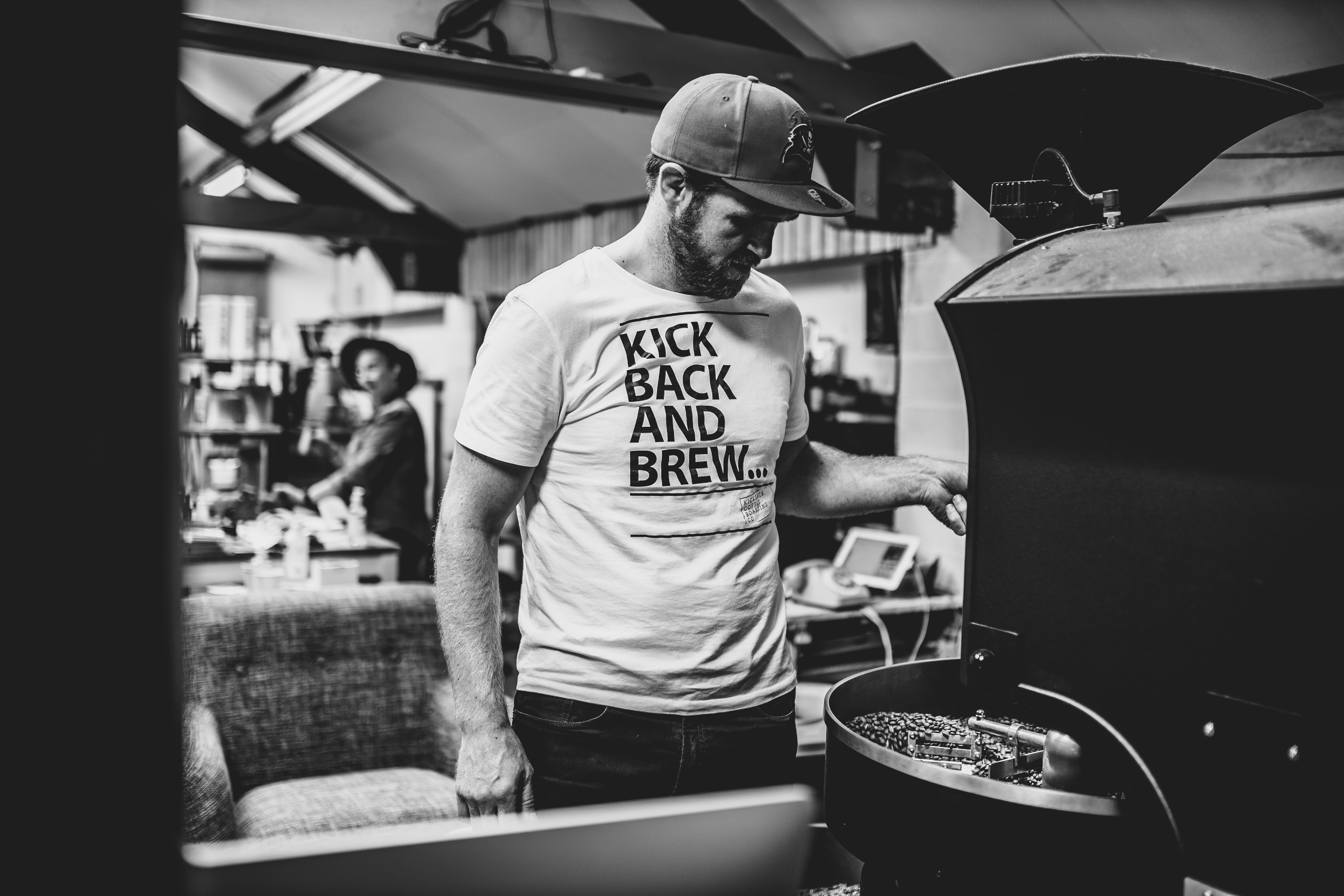 A roaster tending a drum coffee roaster in a roastery
